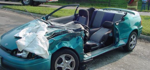 Damaged teal convertible car after accident, deployed airbags, emergency response scene.
