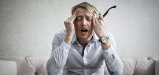 Frustrated man experiencing stress, holding his head with glasses and watch, sitting on sofa.