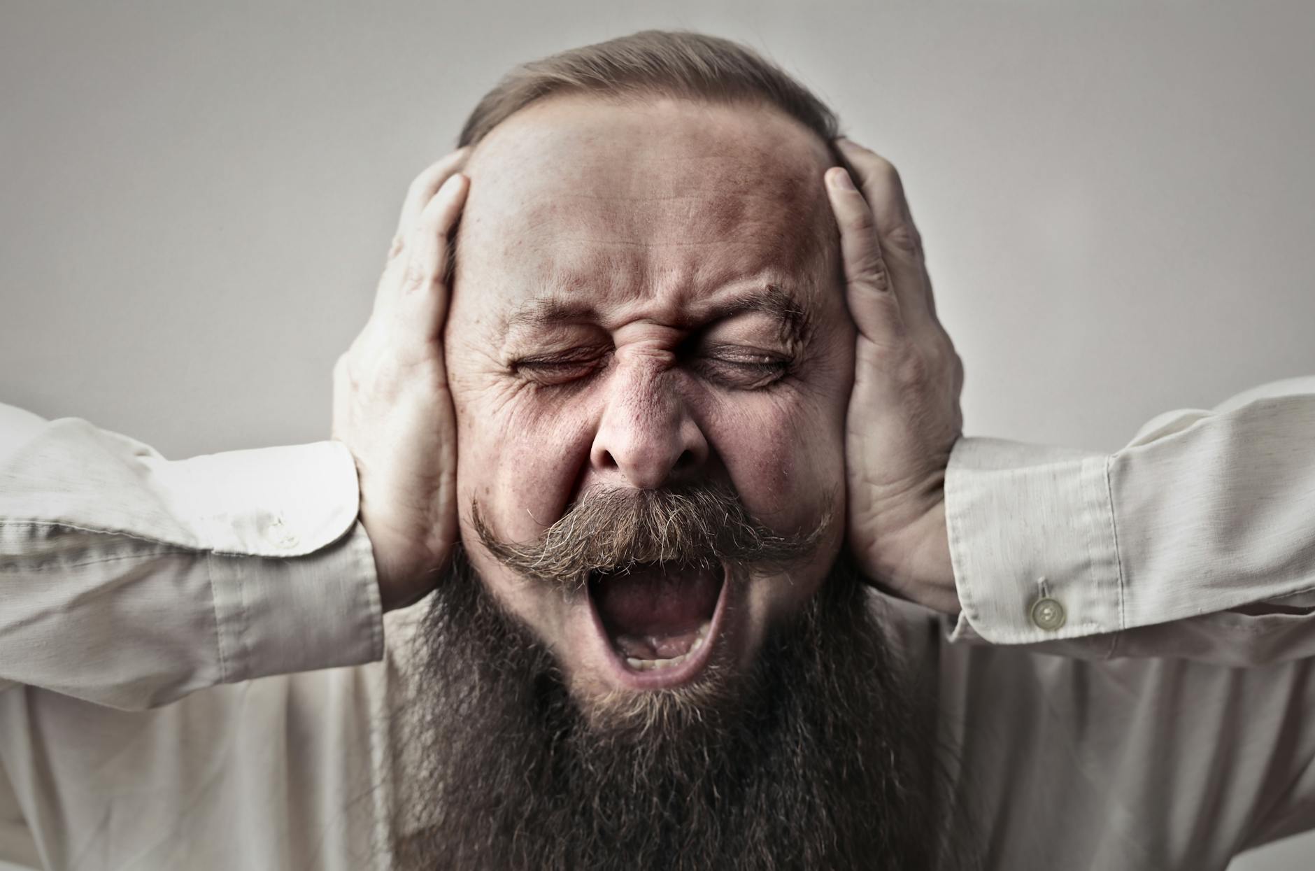 Frustrated man covering ears and shouting, experiencing stress or anger, representing emotional distress and mental health challenges.